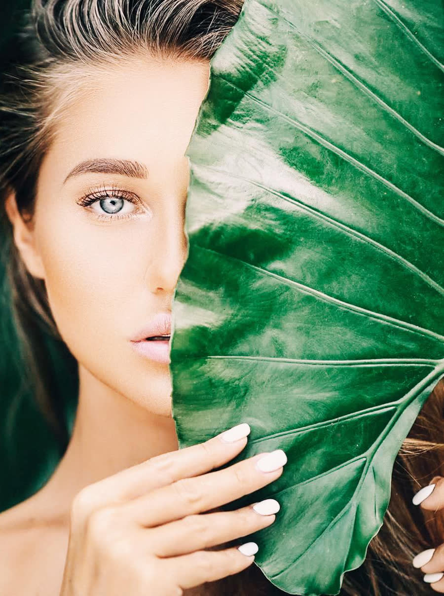 Close-up of a woman's face beside a large green leaf, illustrating healthy, rejuvenated skin
